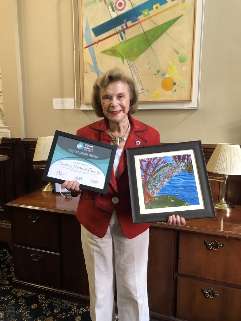 Senator Harriet Chandler holds award and artwork