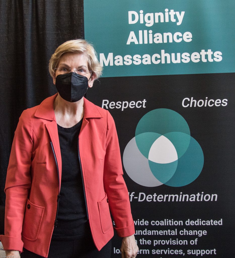 Senator Elizabeth Warren in front of DignityMA banner.